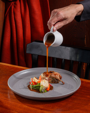 pouring sauce from above on to a grey plate with colorful vegetables and roasted meat