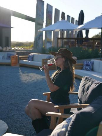 woman wearing a hat sipping wine on a patio with sections of the Berlin Wall behind