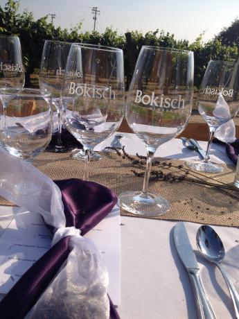 table setting with Bokisch logoed wine glasses.  Vineyards in the background and dark purple napkin