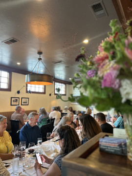 looking into a restaurant dining room men and women seated at a table with pink flowers in the foreground