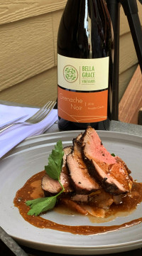 plate of food on a table with a bottle of Bella Grace wine behind it