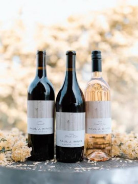 3 bottles of wine sitting on top of a wine barrel.  @ red wines and 1 white wine