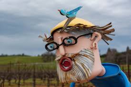 metal sculpture of man with grey beard, glasses and a blue bird on his yellow helmet